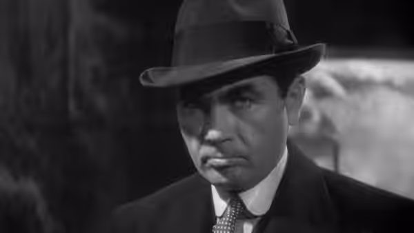 A man in a fedora and dark suit looks ahead