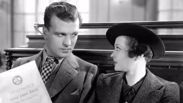 Ted (John Loder) and Mrs. Verloc (Sylvia Sidney) sit together holding a book