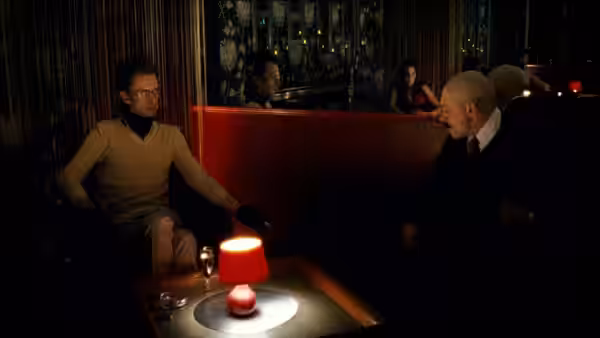 Two men sit opposite each other at a table with a glowing lamp