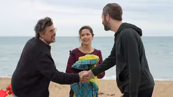 Tucker Crowe (Ethan Hawke) shakes hands with Duncan Thomson (Chris O'Dowd) as Annie Platt watches on the beach