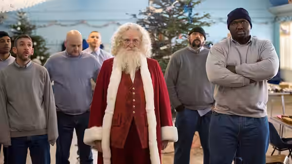 Santa Claus (Jim Broadbent) stands among several men in a room
