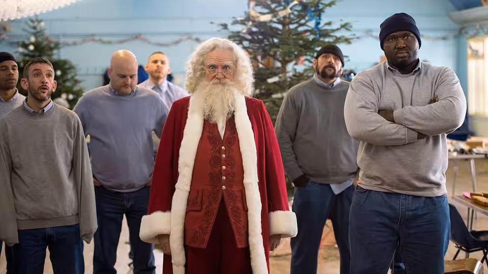 Santa Claus (Jim Broadbent) stands among several men in a room
