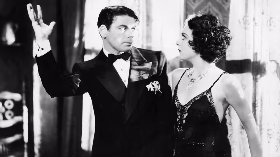 Tony Camonte (Paul Muni) raises a hand beside Poppy (Karen Morley) at a nightclub