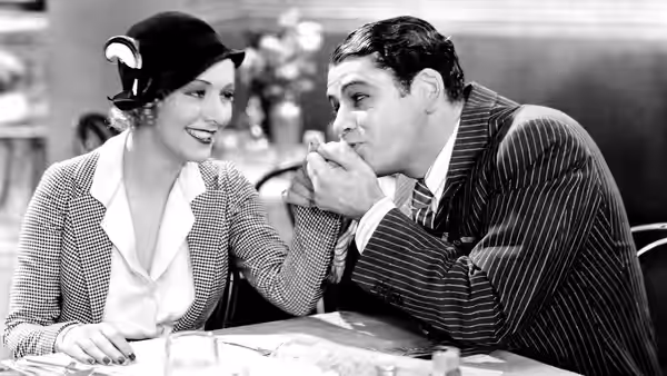Tony Camonte (Paul Muni) kisses Cesca Camonte’s hand at a table