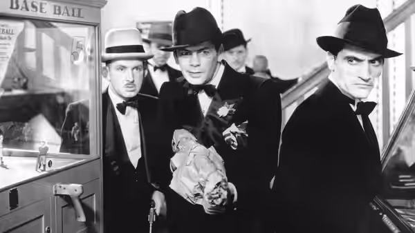 Tony Camonte (Paul Muni) carries a body through a station, flanked by suited men