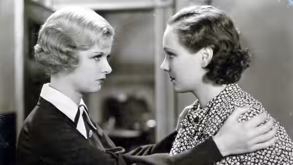 A blonde woman and a brunette face each other, one holding the other's shoulder