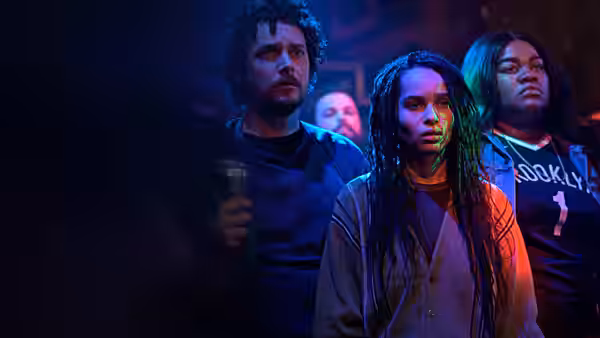 Robyn Brooks (Zoë Kravitz) stands with two companions in blue concert lighting