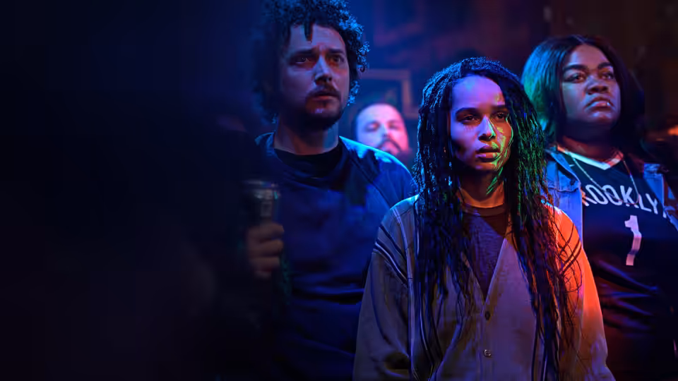Robyn Brooks (Zoë Kravitz) stands with two companions in blue concert lighting