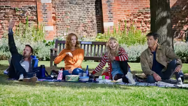 Four friends sit on a picnic blanket outside a brick building