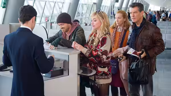 Four travelers queue at an airport counter with passports and luggage