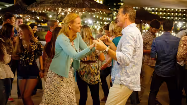 A blonde woman and a man dance together among guests at an evening party