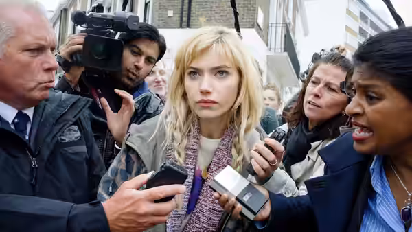 A blonde woman faces reporters and cameras as they crowd around her