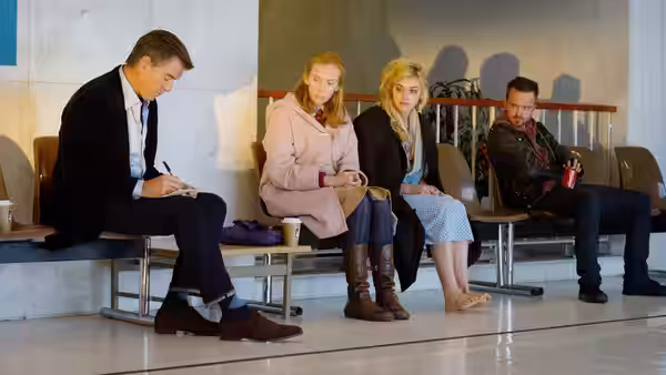 Four people sit in a row of airport seats while a man writes