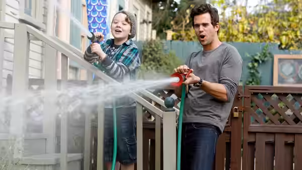 Will (David Walton) stands beside Marcus (Benjamin Stockham) on a porch as Marcus holds a blue object