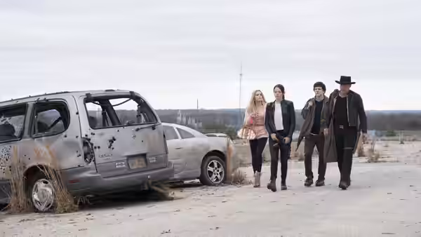 Four travelers walk past a parked RV across a sparse roadside lot