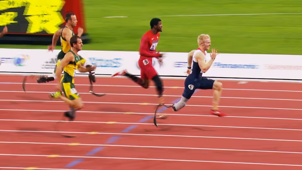 Three track athletes sprint around the red track, one wearing a yellow and green racing kit