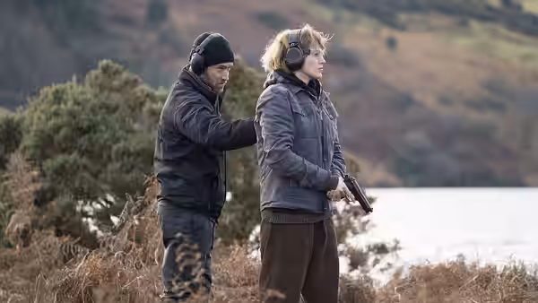 Iain Boyd (Jude Law) adjusts Stephanie Patrick’s (Blake Lively) clothing outdoors as she holds a gun