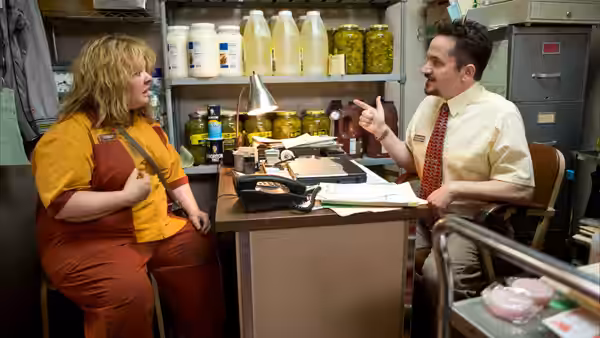 Tammy talks with a man across a desk in a supply room