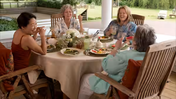 Four women share a meal around a patio table