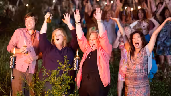 A group of women cheer with raised arms beside a smiling man