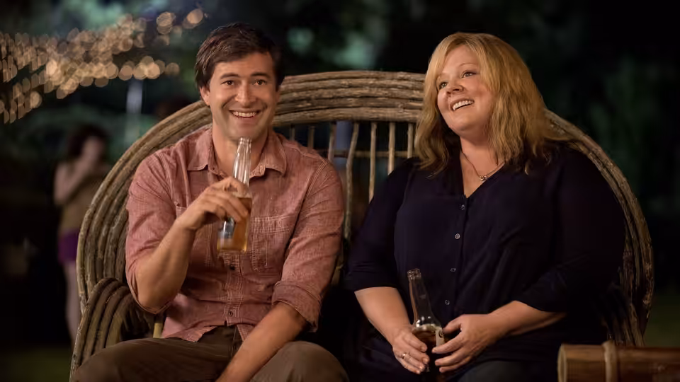 Tammy and a man sit together on a bench, each holding a drink