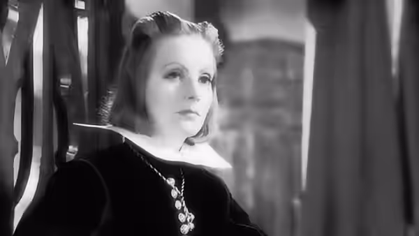 Christina (Greta Garbo) sits in a dark gown and jeweled necklace