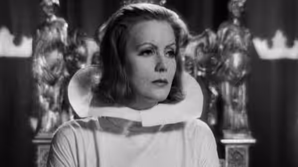 Christina (Greta Garbo) stands before statues in a pale gown