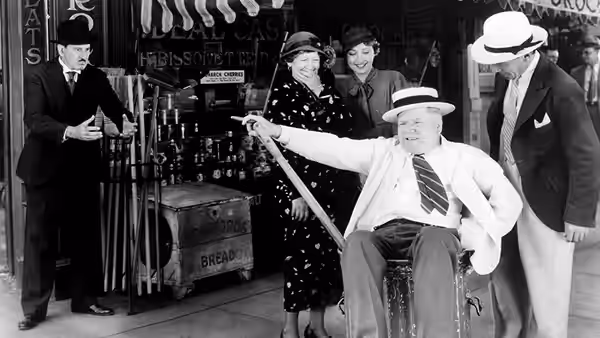 Harold Bissonette (W.C. Fields) sits in a shop, pointing his cane as onlookers gather