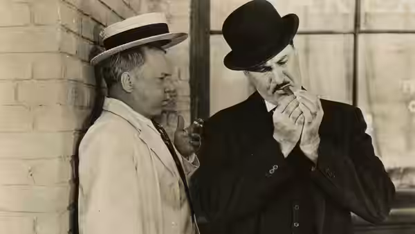 Harold Bissonette (W.C. Fields) stands beside a mustached man lighting a cigar