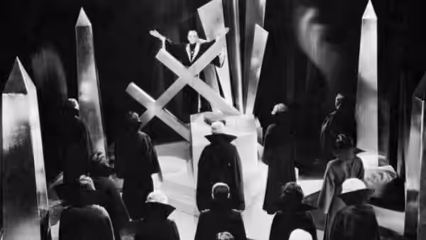 Cult members gather around a geometric altar as an officiant stands above them