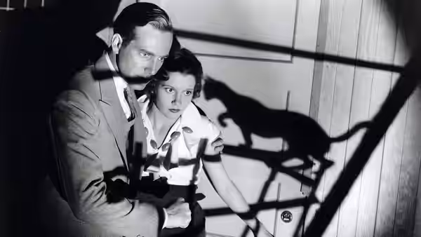Peter Alison (David Manners) holds Joan Alison (Julie Bishop) as shadows fall across the wall