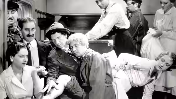 Harpo Marx and fellow passengers crowd into a ship cabin as a steward reaches over them