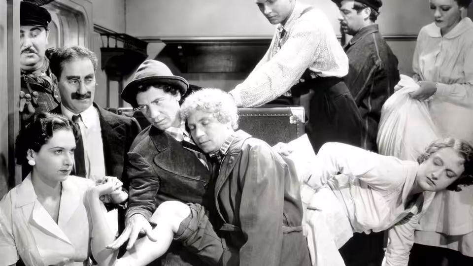 Harpo Marx and fellow passengers crowd into a ship cabin as a steward reaches over them