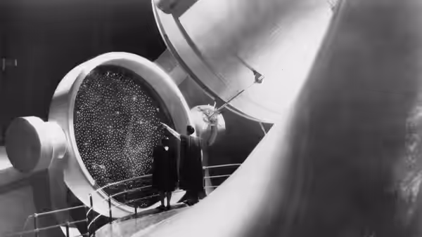 A man stands beside a giant telescope inside an observatory