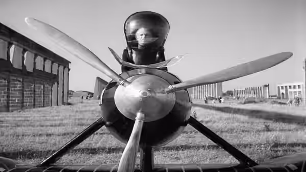 A pilot sits behind an aircraft propeller in an open field