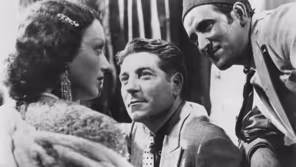 Pépé le Moko (Jean Gabin) sits between a woman and a man leaning close