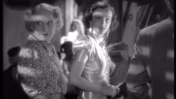 Two elegantly dressed women stand together inside a crowded room