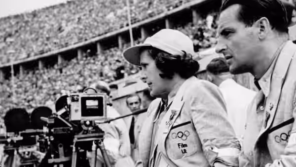 A woman and a man watch a camera crew filming at the stadium