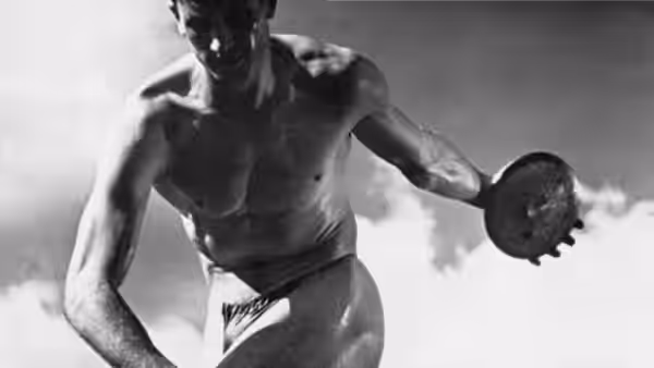 A shirtless athlete holds a discus against the sky