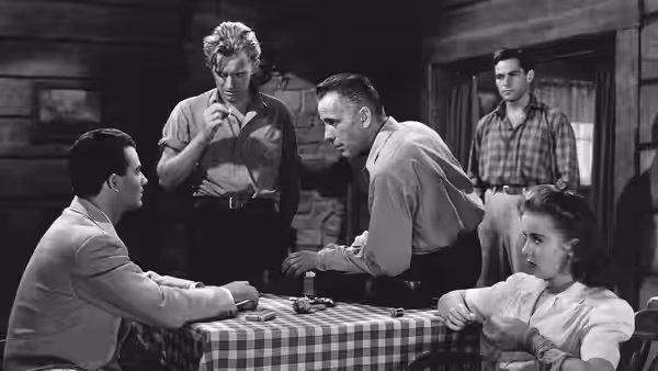 Four people gather around a checkered table, with two men seated opposite each other