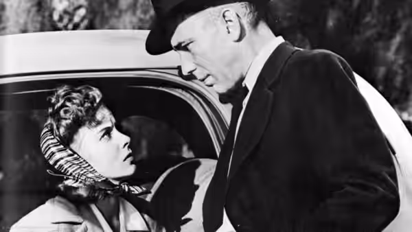Roy Earle (Humphrey Bogart) leans toward a young woman seated in a car