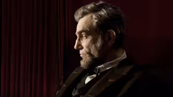 Abraham Lincoln (Daniel Day-Lewis) shown in profile against red curtains