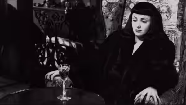 Jacqueline Gibson (Jean Brooks) sits at a table beside a wine glass