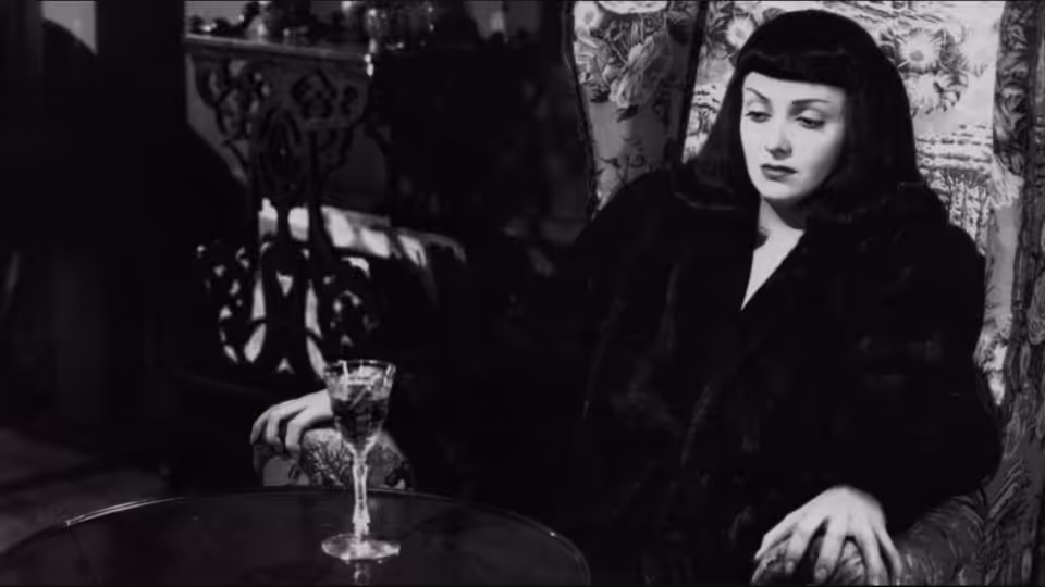 Jacqueline Gibson (Jean Brooks) sits at a table beside a wine glass