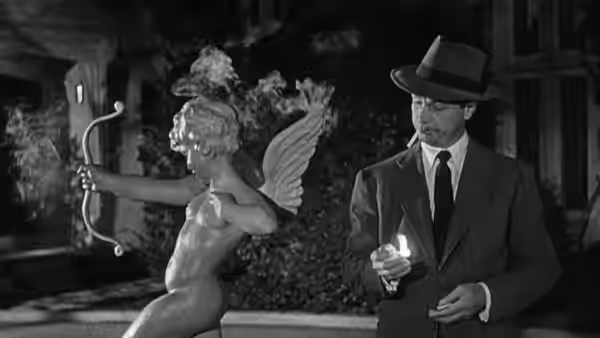 A fedora-wearing man holds a lighter beside a winged cherub statue
