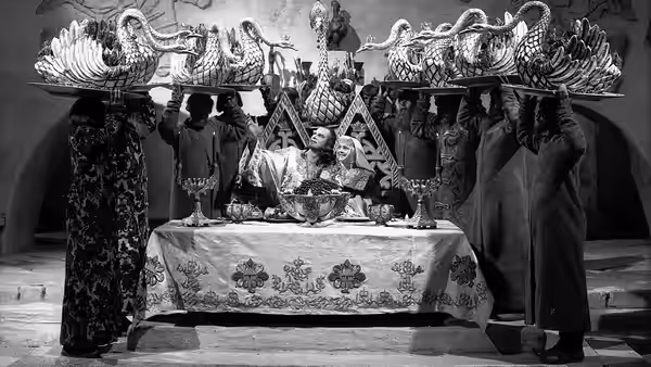 Two men sit at a banquet as attendants hold an ornate dragon overhead