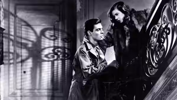 A uniformed man and a woman lean together beside an ornate staircase