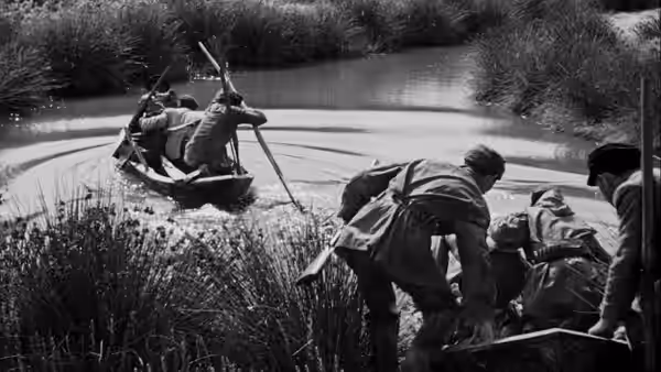 Soldiers wade through reeds beside a small boat crossing a river