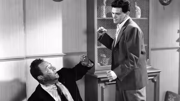 Frank Chambers (John Garfield) stands over Nick Smith (Cecil Kellaway), who gestures up at him