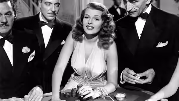 Gilda (Rita Hayworth) sits at a gaming table between tuxedoed men